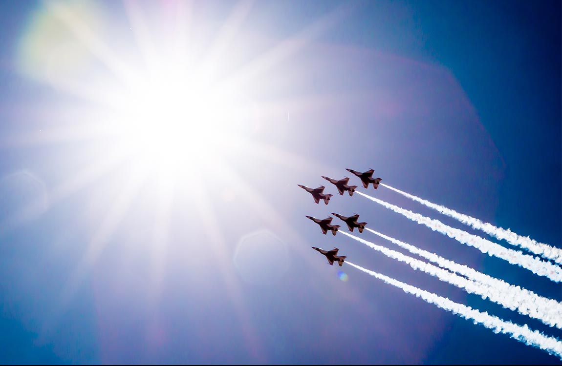 Six fightere jets in formation fly upwards towards the sun 