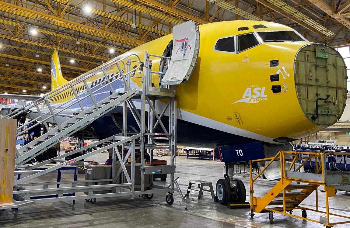 A yellow Boeing 737NG aircraft being dismantled for parts inside a hanger 