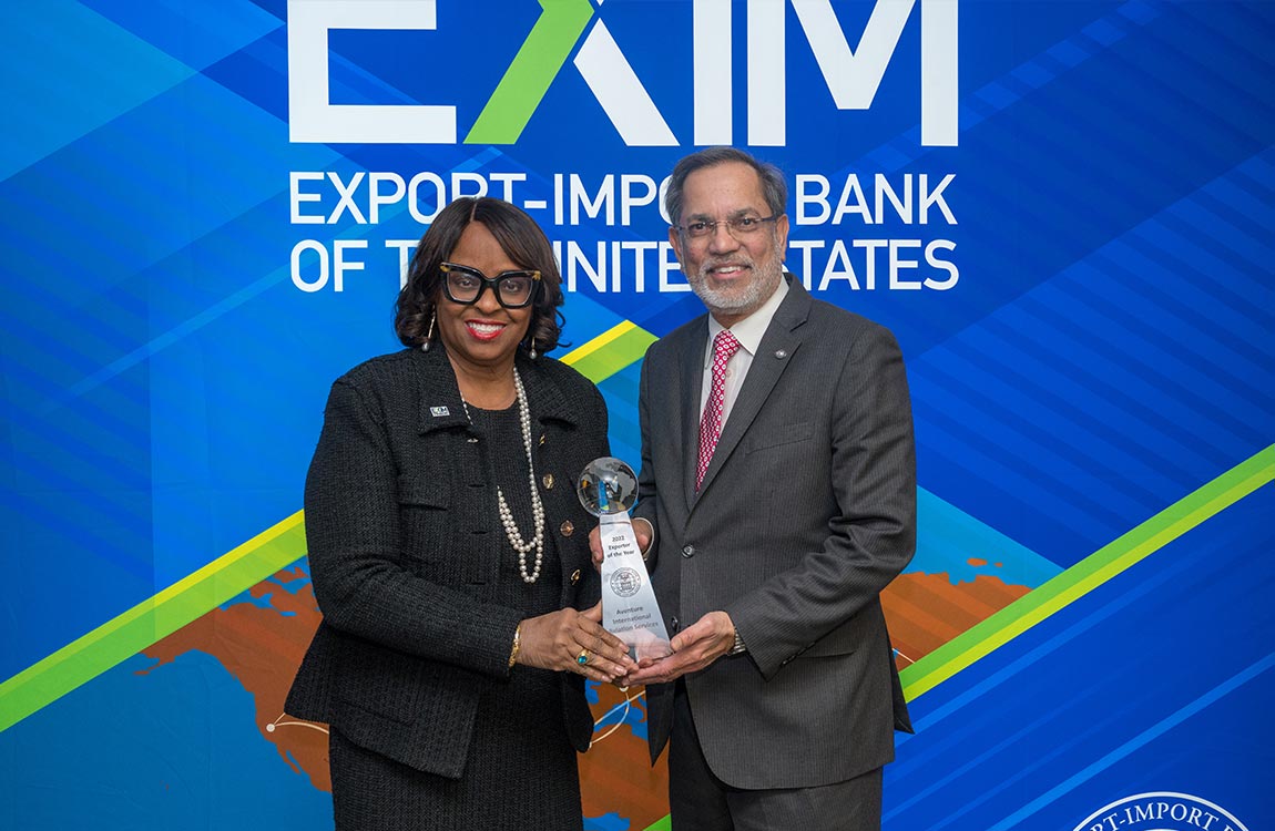 A woman presents an award to a man in front of a backdrop that says EXIM Export-Import Bank of the United States 