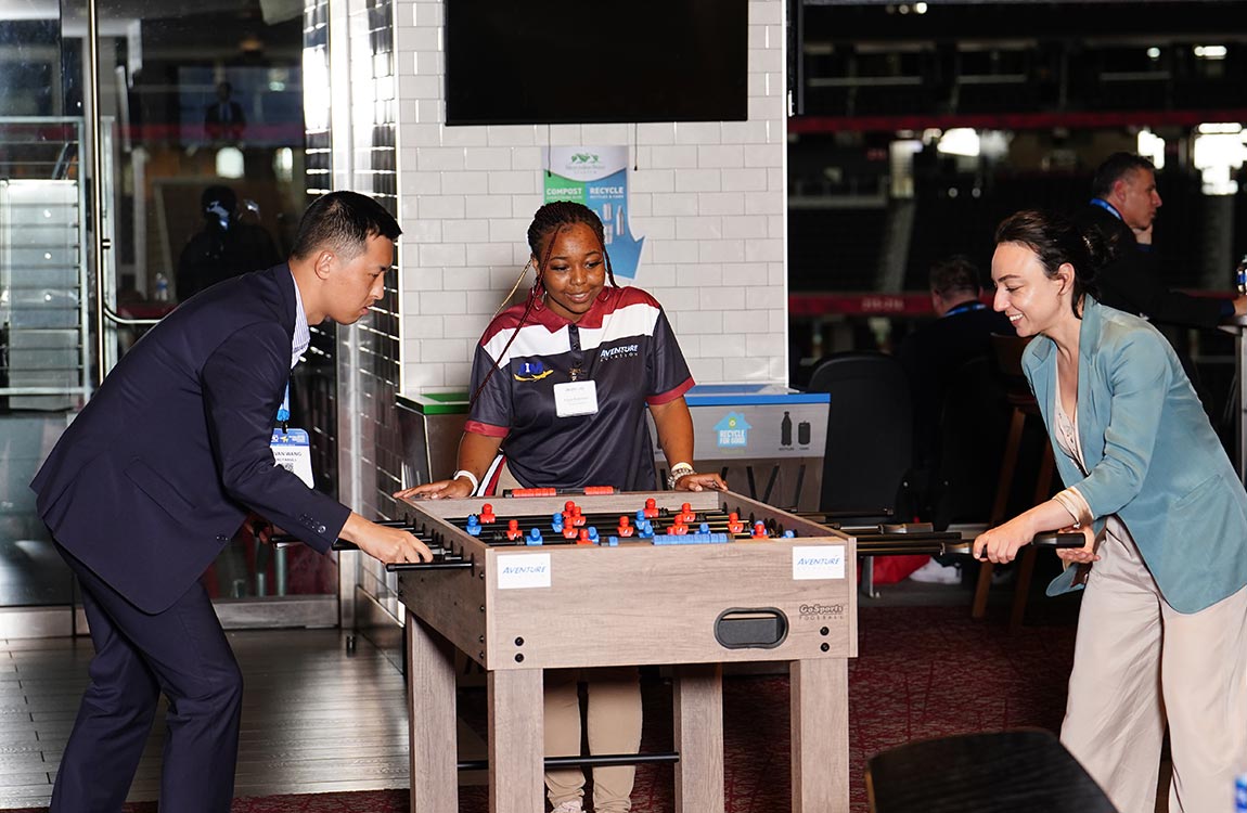 Man and woman play foosball, while a women in the center looks on 