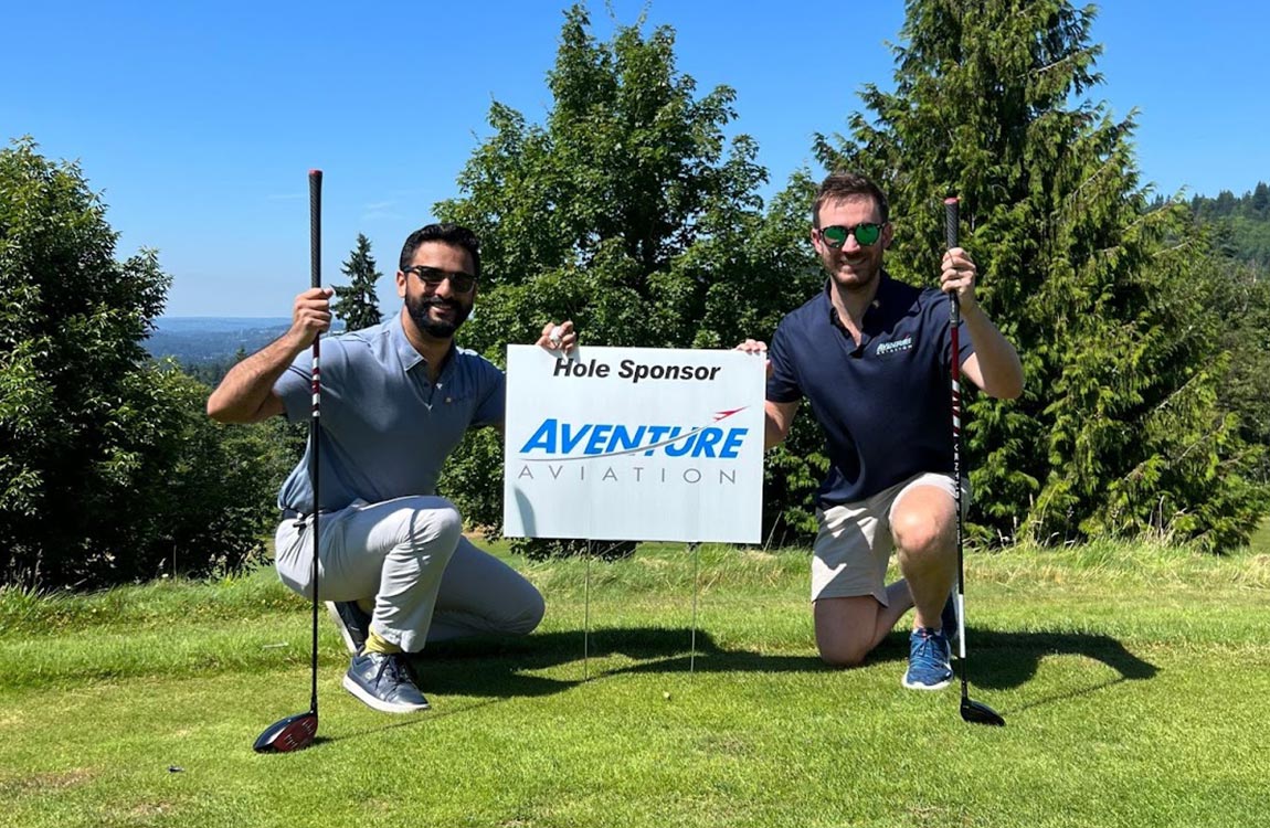Two men on a golf course holding a sign saying "Hole Sponsor Aventure Aviation" 