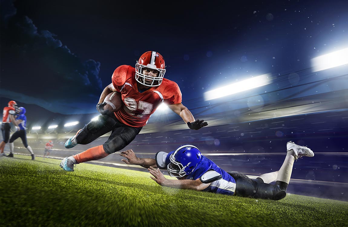 An American football player running with the ball avoids benig tackled while playing a nightgame in an open air stadium 