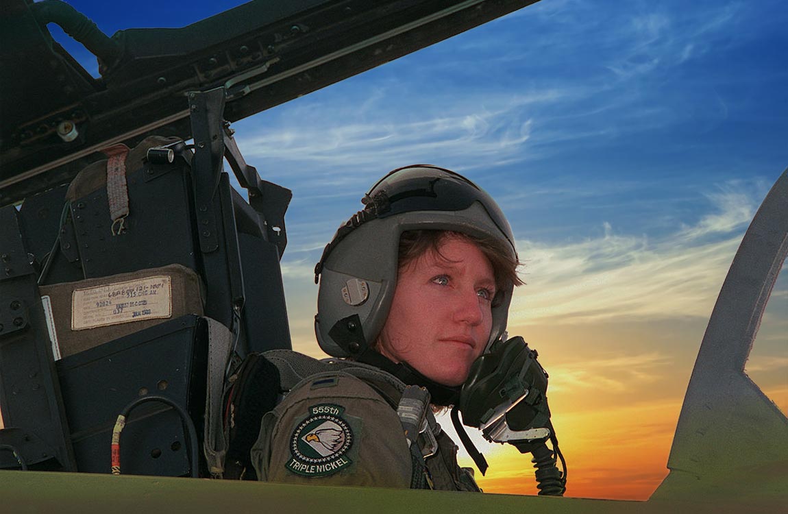 Woman in the cockpit of a fighter jet on the ground, with a brilliant blue and orange sky 