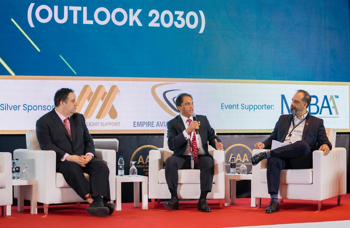 Three men in suits sitting in chairs on a stage, engaged in discussion 