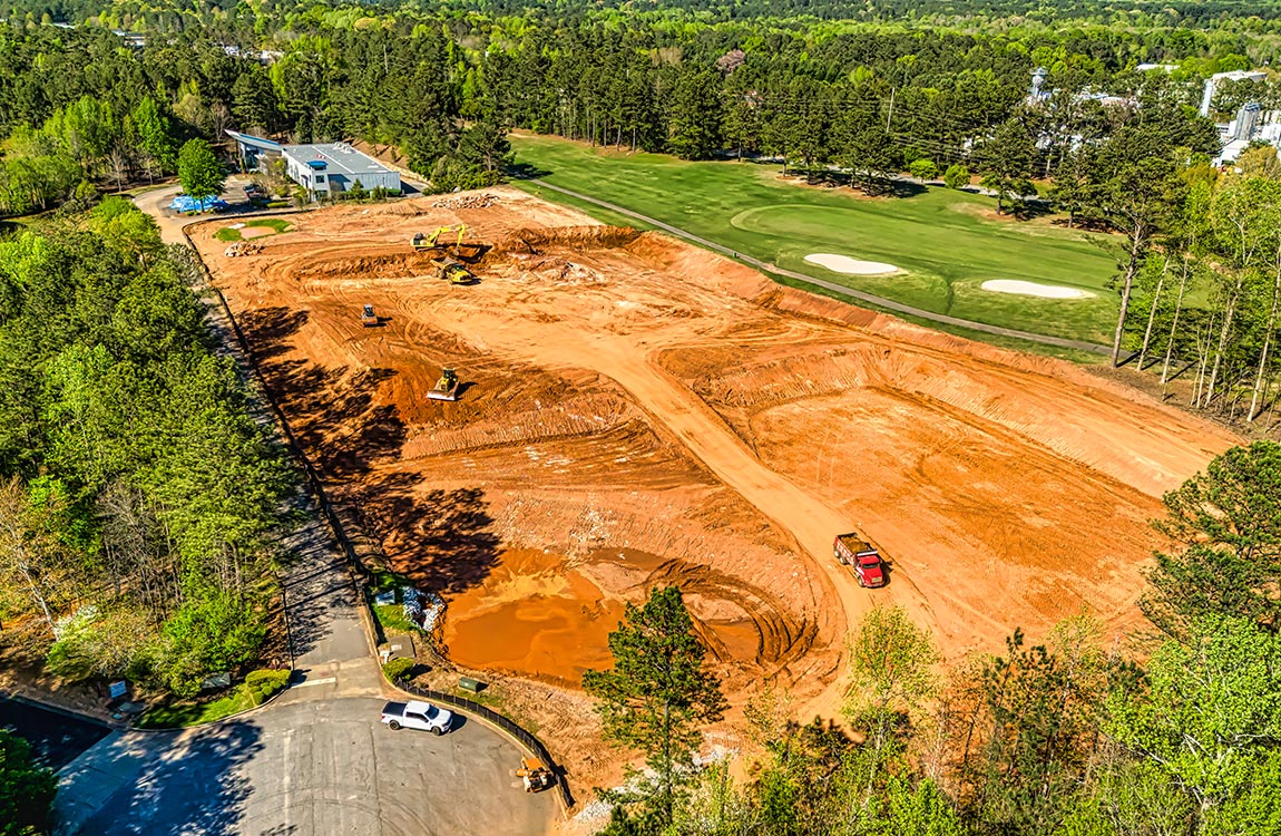 Aerial view of a large amount of land being cleared by tractors and trucks, next to a golf course 