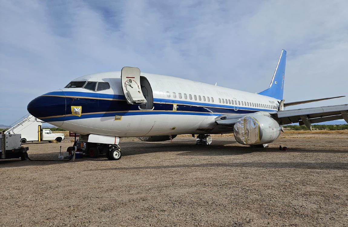 Commercial airplane in the desert with door open and engine covered, with a blue sky above 