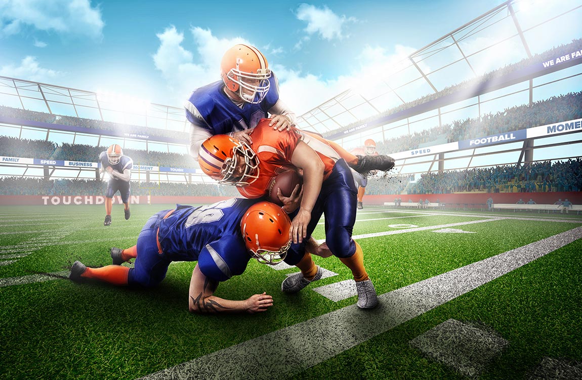 An American football player being tackled by two other players in an outdoor stadium under a blue sky 