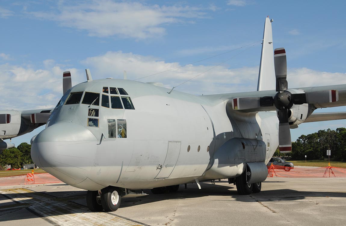 Close up of a C-130 military transport aircraft on the tarmac, under a blue sky 