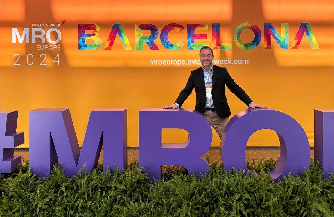 A man poses behind of a sculpture of large letters saying "MRO," with a sign in the background saying "Aviation Week MRO Europe 2024 Barcelona" 