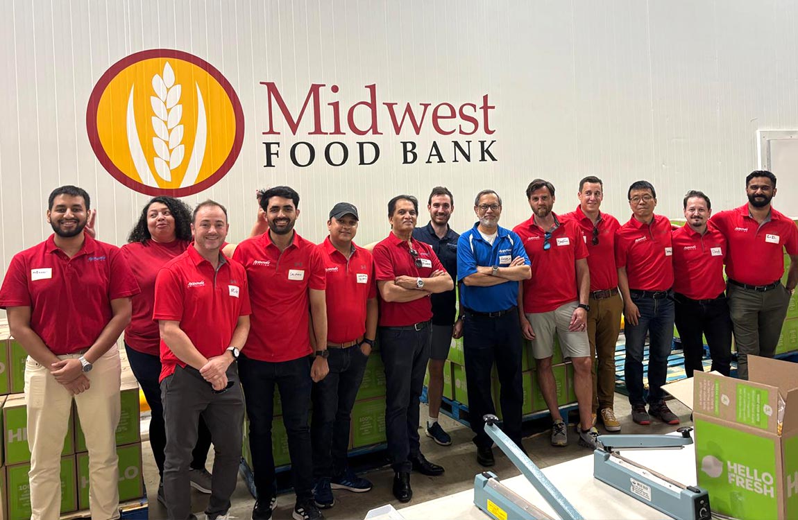 13 people in shirts saying "Aventure Aviation" in a food distribution center,  below a sign saying "Midwest Food Bank" 