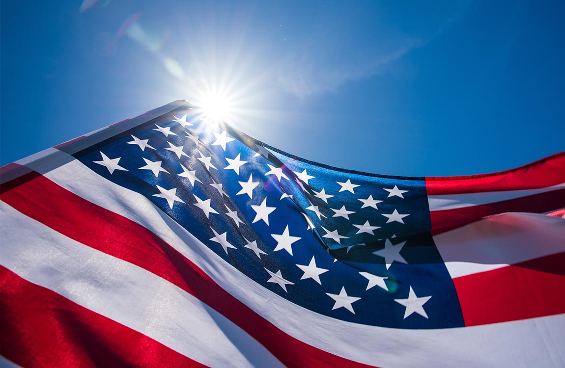 Large America flag flying in front of a bright blue sky 