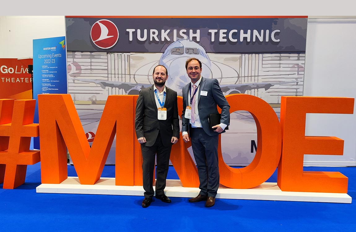 Two men in business suits at a trade show stand next to large 3D letters saying #MROE, in front of a sign saying Turkish Technic 