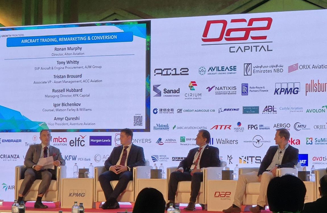 Four men on a large stage with a huge background full of corporate logos 