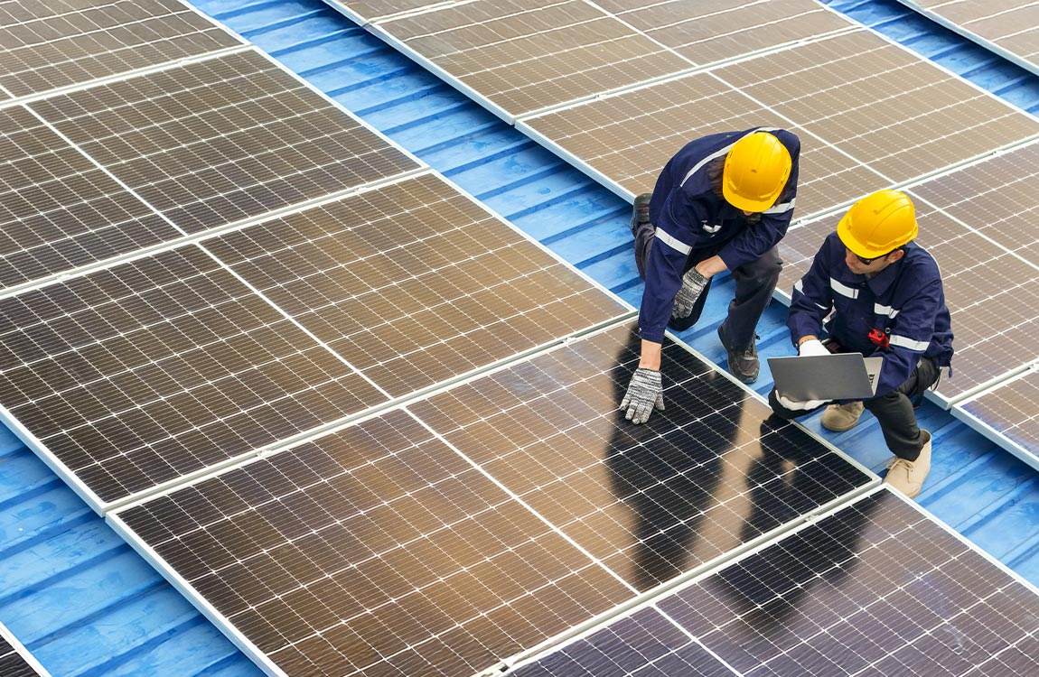Two workmen on a roof inspecting solar panels 